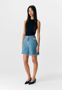 Shorts en denim avec une coupe décontractée, couleur bleu clair, ourlet effiloché et design à cinq poches. Associés à un haut noir ajusté sans manches et des chaussures noires à talons pointus.