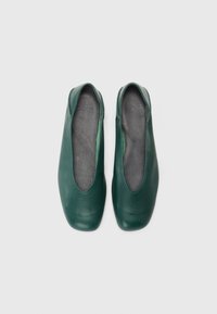 Sapatos slip-on verdes de couro com bicos arredondados e uma textura suave, apresentando um interior forrado suave. Design minimalista, sem adornos.