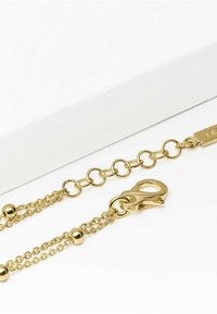 Bracciale in oro con maglie intrecciate, piccole perline rotonde e chiusura a moschettone. Texture liscia con una finitura lucida.