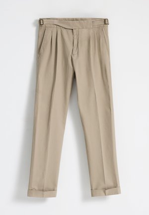 Pantalones beiges con pliegues y textura suave, que cuentan con una cinturilla con cinta, bolsillos laterales y dobladillos con vuelta.