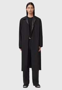 Zwarte lange jas met knoopsluiting en een puntkraag, gemaakt van een gladde, gestructureerde stof en een minimalistisch ontwerp.