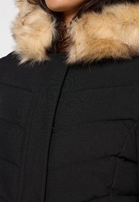 Czarna kurtka puchowa o pikowanej strukturze z odpinanym beżowym kołnierzem z sztucznego futra. Posiada eleganczne frontowe zapięcie oraz boczne kieszenie.