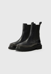 Bottines Chelsea en cuir noir avec des panneaux élastiques sur les côtés et des détails métalliques texturés le long de la semelle intermédiaire ; semelle en caoutchouc noir robuste.