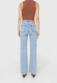 Džíny s vysokým pasem, světle modré denimové, s rovnými nohavicemi, které mají dvě zadní kapsy a hnědou koženou značkovou štítek na pasu.