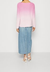 Gebreide trui met een roze naar witte gradient, gecombineerd met een lichtblauwe denim maxi rok. De schoenen zijn witte sandalen met blokhak.