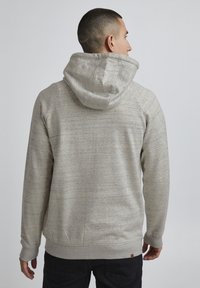 Hanorac gri deschis dintr-un material texturat, cu aspect heather, având o glugă mare, mansete ribate și o margine la talie. Fără marcaje vizibile.