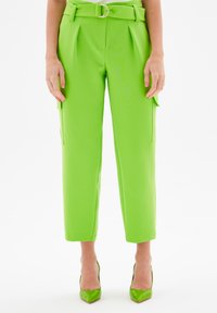 Felgroene op maat gemaakte broek met plooien, een riem met een ronde gesp en zijzakken. Gladde textuur en cropped lengte.