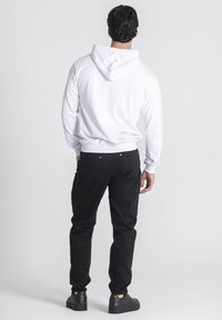 Sudadera blanca con capucha, puños y dobladillo acanalados, combinada con pantalones negros que cuentan con bolsillos traseros y detalles de hardware en plata.