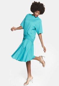 Turkusowy dwuczęściowy zestaw składający się z bluzki z krótkim rękawem i spódnicy do kolan, wykonany z miękkiego materiału o płynnej teksturze.