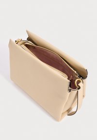 Smėlio spalvos odinė rankinė su auksine užtrauktuku, rausvos spalvos vidiniu pamušalu ir nuimama rankena su auksiniais žiedais, šonu matoma baltoje fone.