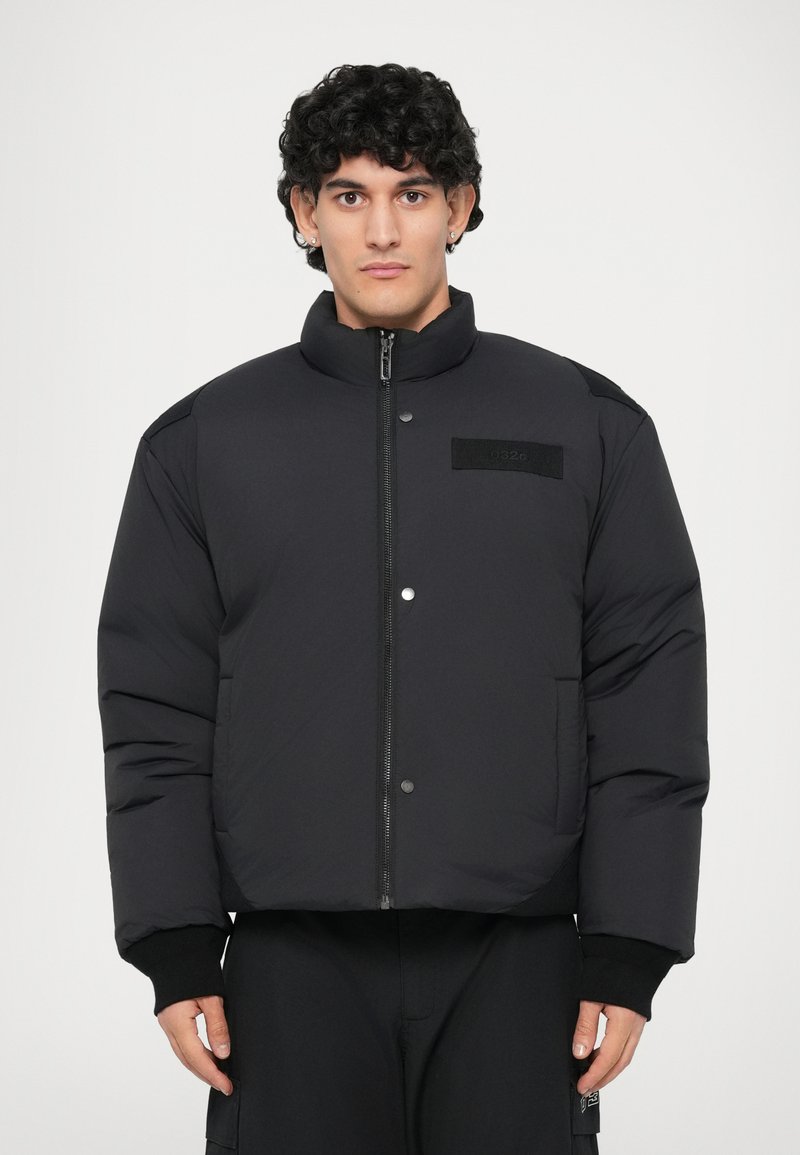 Schwarze Steppjacke mit hohem Kragen, Reißverschluss vorne und zwei seitlichen Taschen. Verfügt über ein strukturiertes Patch und gerippte Bündchen, aus einem glatten Material gefertigt.