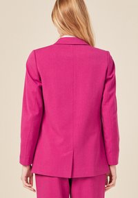 Roze op maat gemaakte blazer met lange mouwen en gesneden revers, met een getailleerd ontwerp, achterste uitsparing en een gladde textuur.
