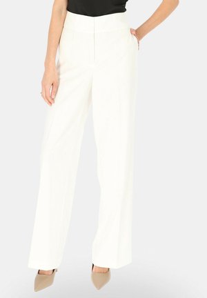 Kobieta ubrana w białe szerokie spodnie z wysokim stanem i kieszeniami, zestawione z czarnym topem i beżowymi szpiczastymi szpilkami.