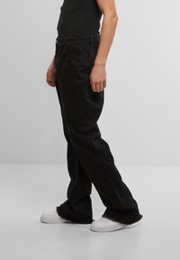 Pantaloni din denim negri cu croiala dreaptă, buzunare vizibile și tiv desfăcut. Stilizați cu un top simplu negru și adidași albi.
