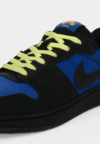 Μαύρο και μπλε παπούτσι Nike SB με κίτρινα κορδόνια, μαύρο λογότυπο swoosh και "Nike SB Code 58" στην μπλε ετικέτα της γλώσσας.