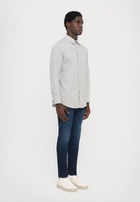 Lys grå skjorte med små svarte prikker, parret med mørkeblå jeans og hvite sneakers, som står mot en hvit bakgrunn.