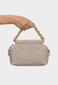 Beżowa torebka o fakturze z puchową konstrukcją, z złotym łańcuchowym uchwytem. Szczegóły zamka błyskawicznego z boku. Gładki, miękki materiał.