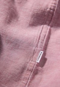 Rosa linne tyg med en slät textur, som har en sydd söm och en vit etikett som visar märket "Lindbergh."
