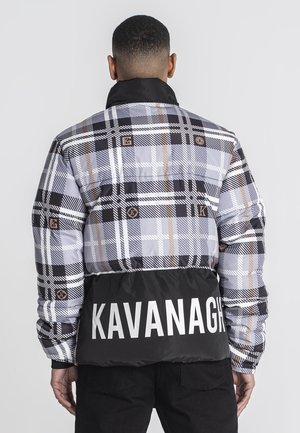 Mann trägt eine schwarz-grau-weiße Karojacke mit einem schwarzen unteren Abschnitt, auf dem das Wort KAVANAGH in großen weißen Buchstaben steht.