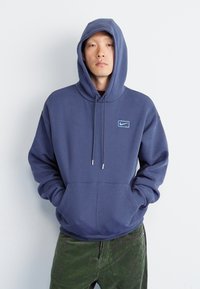Navy blue hoodie made of soft fabric, featuring a front pocket, drawstrings, and a small light blue Nike logo on the chest.