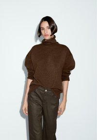 Brown oversized turtleneck sweater with ribbed texture, paired with dark green high-waisted pants featuring a front button and pockets.