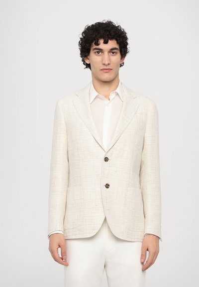 Blazer in lino beige chiaro con un motivo testurizzato, design a un bottone, due bottoni e revers a punta indossato sopra una camicia bianca.