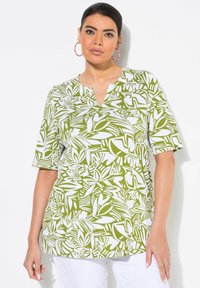 Blusa de estampado verde y blanco con mangas cortas, diseño de cuello en V, que presenta un print de hojas sobre una tela suave. Combinada con pantalones blancos.