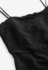 Robe noire avec des motifs floraux brodés sur le corsage, bretelles spaghetti ajustables et jupe à texture lisse.