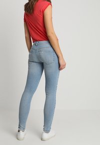 Jeans skinny azul claro con cintura alta, con bolsillos traseros y un lavado desgastado, combinados con una camiseta roja de manga corta y zapatillas blancas.