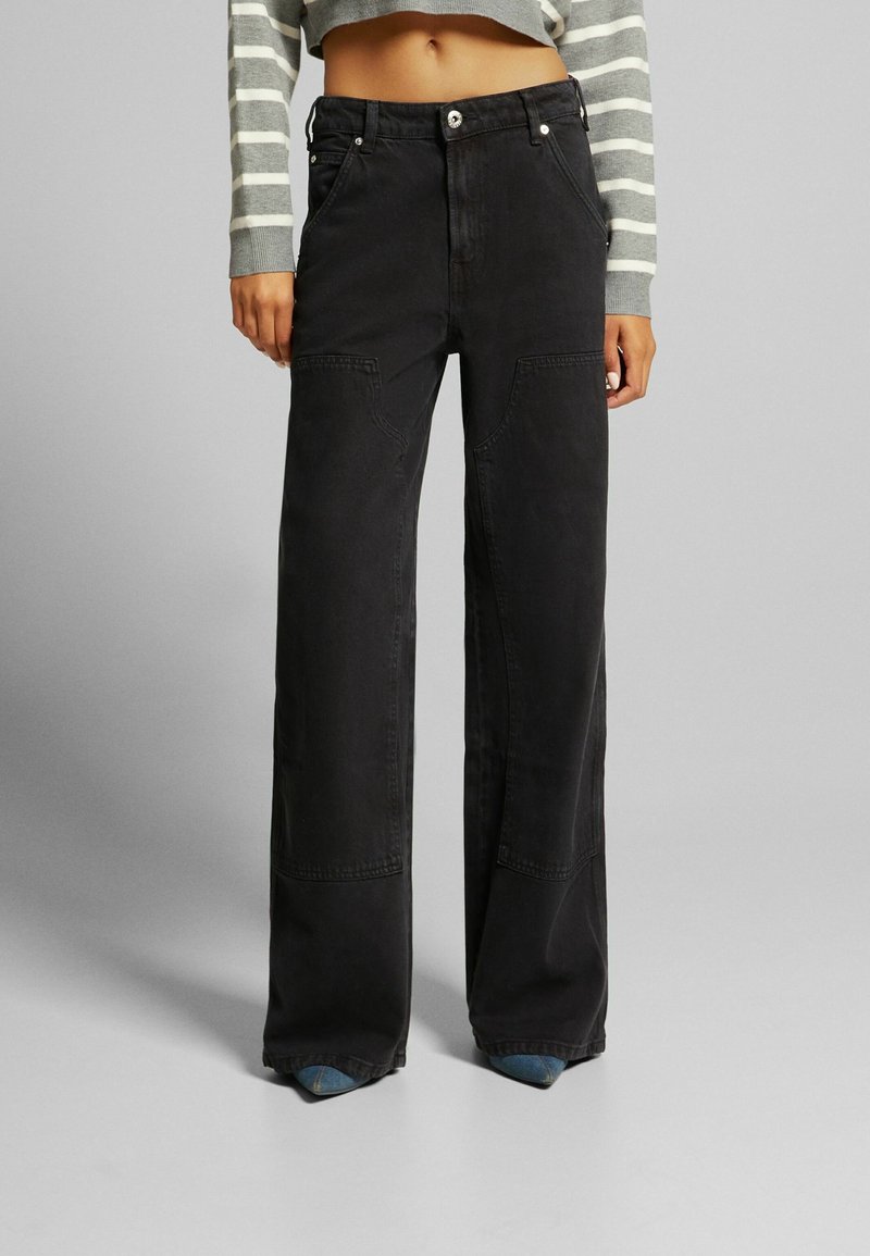 Pantalons en denim noir à jambes larges avec poches avant doubles, quincaillerie argentée et accents bleus contrastés à l'ourlet. Texture lisse et design décontracté.