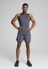 Grå ärmlös atletisk topp och matchande shorts i lättviktsmaterial, med en logotypdetalj. Svarta sportskor fulländar outfiten.