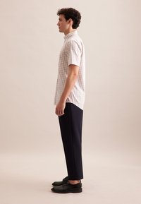 Camicia a maniche corte a quadretti in rosa chiaro e bianco, abbinata a pantaloni blu navy e scarpe in pelle nere, mostrata di lato.