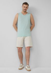 Helles blaues ärmelloses Tanktop, beiger Shorts und beiger Sneakers mit einer cremefarbenen Sohle. Einfaches Design, lockere Passform und weicher Stoff.