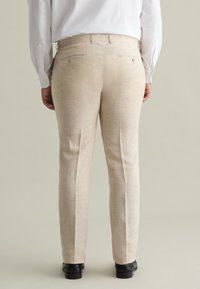 Beige linnen broek met een rechte pasvorm. Bevat twee achterzakken en een subtiele textuur. Gecombineerd met zwarte schoenen.