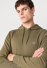 Olijf groene hoodie van een gestructureerde stof, met een trekkoordcapuchon en een klein vierkant BOSS-logo op de borst. Ontspannen pasvorm met lange mouwen.