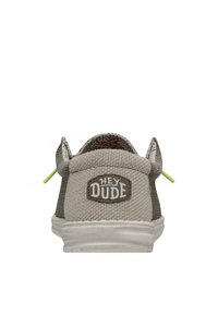 Zapatillas slip-on de lona gris claro con una superficie texturizada, acentos verdes y un parche de logo bordado en el talón. Suela de goma.