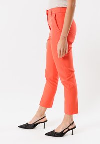 Pantaloni tailored color corallo con una trama liscia, pieghe davanti e taglio cropped, abbinati a décolleté slingback nere a punta.