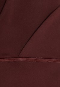 Gros plan sur un tissu rouge foncé lisse avec une couture visible et un détail de surpiqûres fines.