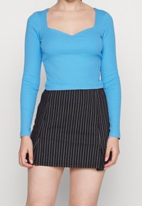 Blå, långärmad ribbad topp med fyrkantig halsringning, ihop med en svart randig kjol med en sidopenna.