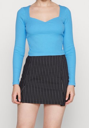Blaues, langärmliges Rippoberteil mit quadratischem Ausschnitt, kombiniert mit einem schwarzen, gestreiften Rock mit seitlichem Schlitz.
