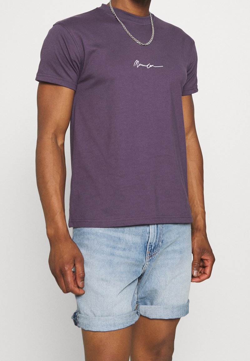 Fialové bavlněné tričko s krátkým rukávem a kulatým výstřihem, na hrudi s bílým vyšívaným nápisem. Kombinováno se světlými modrými denimovými šortkami.