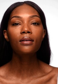 Gros plan sur une personne à la peau lisse et chaude, aux longs cheveux sombres et au maquillage naturel, mettant en valeur des lèvres pleines et des pommettes bien définies.