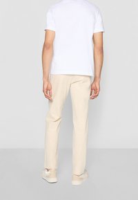 Witte T-shirt met korte mouwen en ronde hals, gecombineerd met lichtbeige broek en beige sneakers. Minimalistisch ontwerp met een relaxte pasvorm.