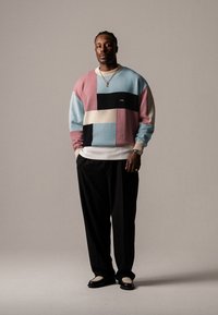 Pullover colorato lavorato a maglia con blocchi di rosa, blu, nero e crema, abbinato a pantaloni neri e scarpe con dettagli in rete.