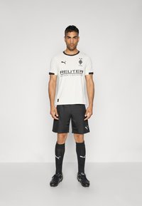 Hvid fodboldtrøje med korte ærmer, sorte detaljer og logo, parret med sorte shorts og knælange sorte sokker med hvidt logo, sorte fodboldstøvler.