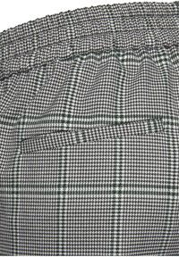 Grijs-wit geblokt stof met groene accenten, met een elastische tailleband en een achterzakdetail. Getextureerd geweven patroon.