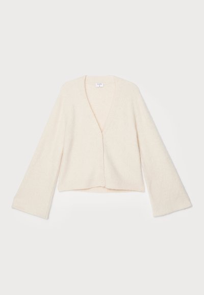 Kreminės spalvos megztinis su V formos iškirpte, ilgomis varpo formos rankovėmis ir keturiais mygtukų užsegimais. Minkšta tekstūra, trumpas dizainas, be matomų raštų.