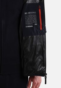 Blå isoleret jakke med en blank sort indvendig. Har en orange lynlåslomme med et mærke, der detaljere 20-22 serien.