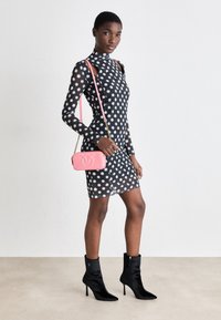 Abito nero a pois con collo alto e dettagli cut-out, abbinato a una borsa a tracolla rosa e stivaletti neri alla caviglia con punta appuntita.