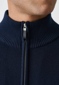 Granatowy sweter zapinany na zamek z prążkowanym kołnierzem, charakteryzujący się wysoką szyją i gładką teksturą dzianiny, srebrnym zamkiem błyskawicznym oraz minimalistycznym designem.